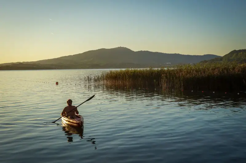 Lone kayaker paddling across a calm lake at sunset with hills behind