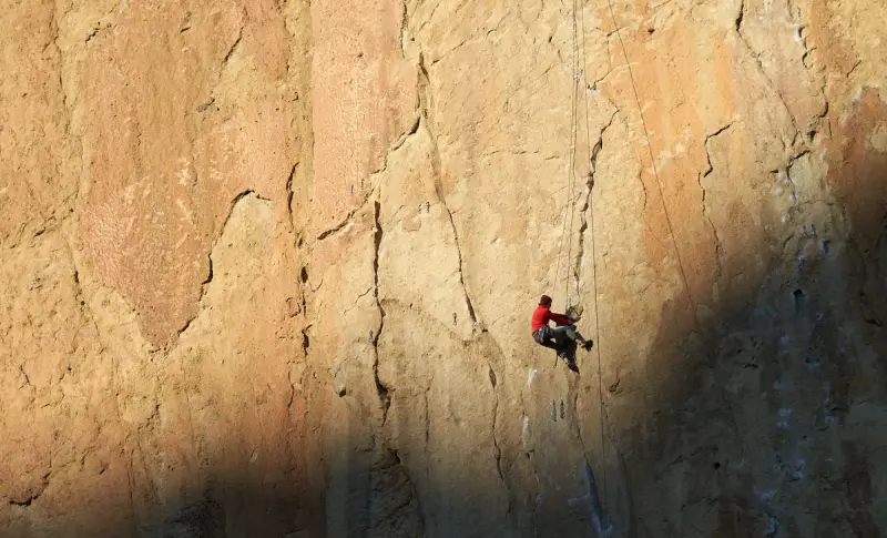 Climber in red high on a tall sunlit sandstone wall