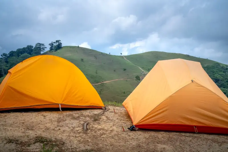 Two bright orange dome tents pitched on a grassy hilltop under clouds