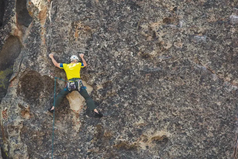 Helmeted climber in a yellow shirt scaling a rough granite face