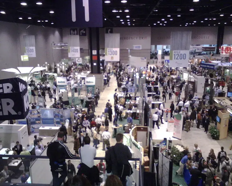 Crowded Greenbuild Expo aisles seen from above, with numbered aisle banners and exhibit booths