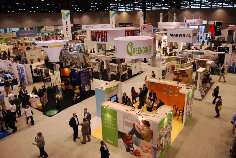 Busy Greenbuild exhibit hall with hanging banners, island booths and attendees walking between exhibits