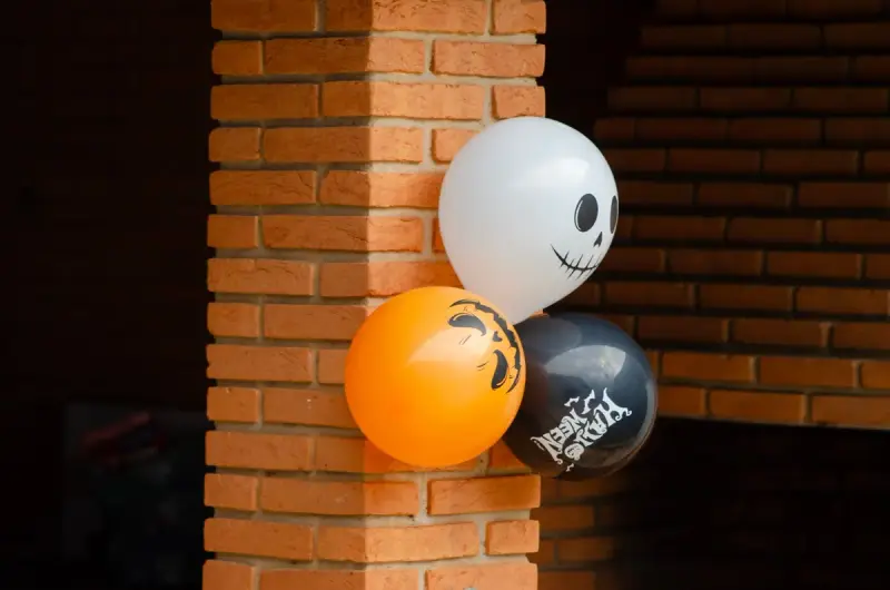White, orange and black Halloween balloons with spooky faces tied to a brick column