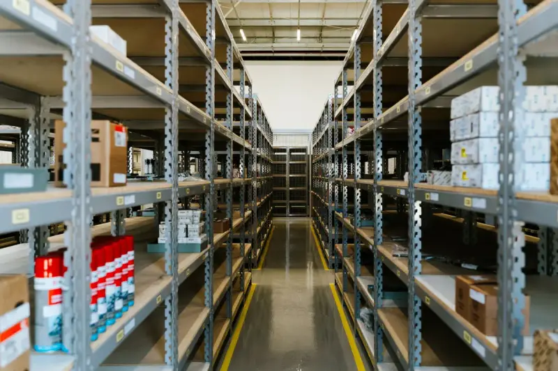 Narrow aisle between tall metal shelves of boxed stock in a distribution warehouse