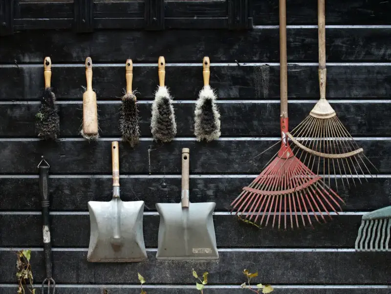 Garden rakes, shovels and brushes hanging neatly on a dark wooden wall