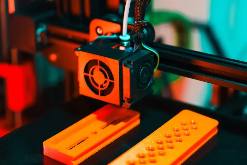 3D printer extruding orange plastic parts for a prototype