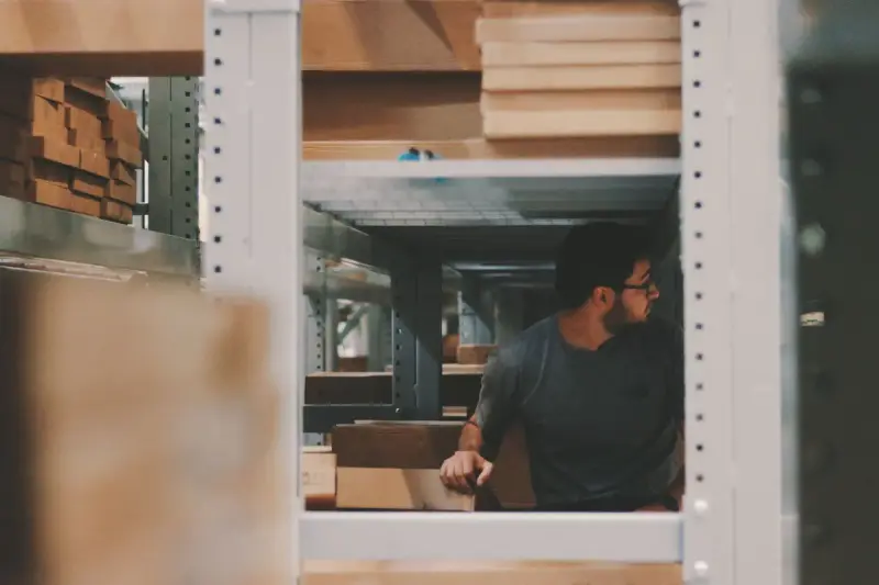 Man stacking wooden planks on high warehouse shelving