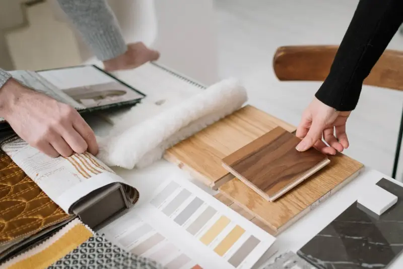 Hands comparing wood plank and textile samples for an interior finish scheme
