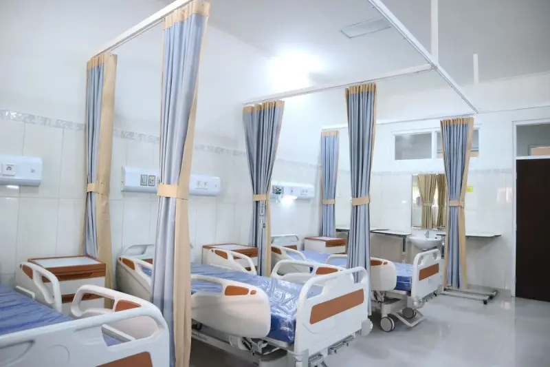 Hospital ward with beds separated by privacy curtains on ceiling tracks