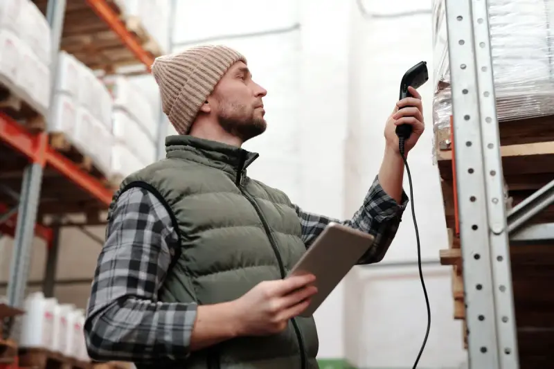 Warehouse worker scanning shelf stock with a handheld scanner and tablet