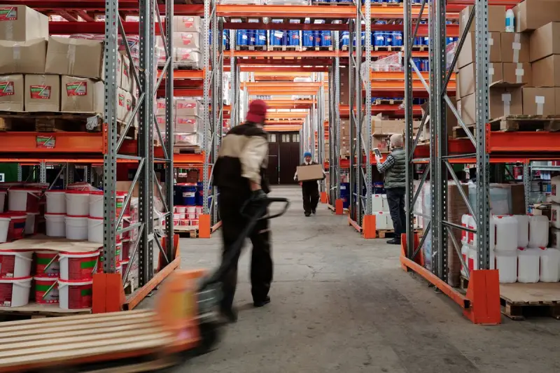 Warehouse staff moving goods with a pallet jack between full storage racks