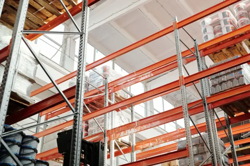 Looking up at orange pallet racking under a bright warehouse skylight