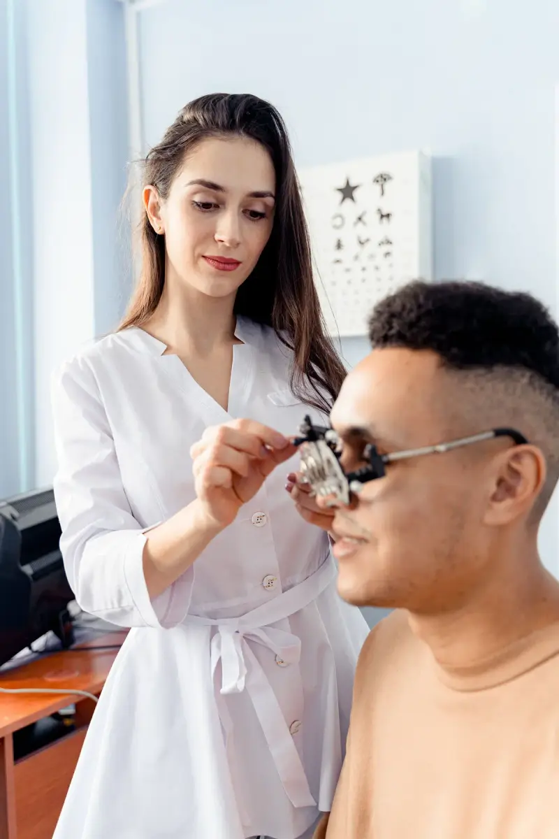 Optometrist fitting a trial lens frame on a patient beside an eye chart
