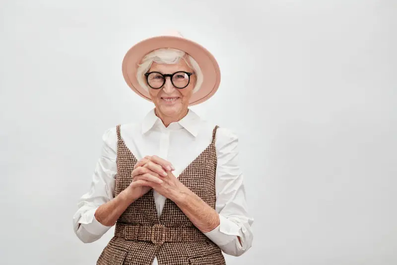 Stylish older woman in round eyeglasses, a pink hat and a tweed vest