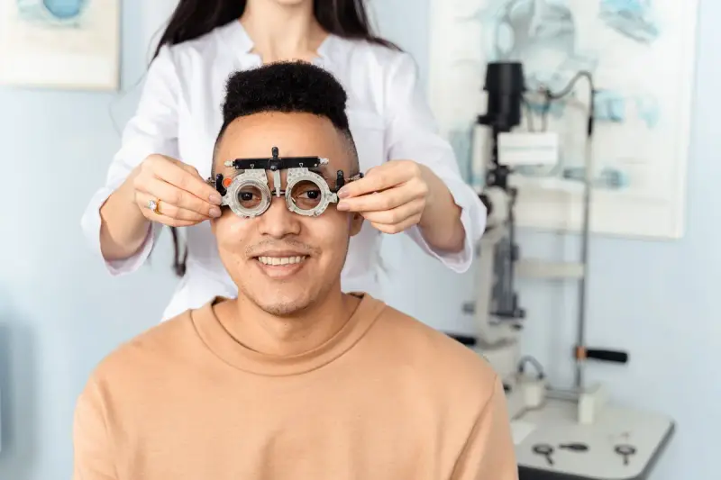 Optometrist placing a trial frame on a smiling patient in an exam room