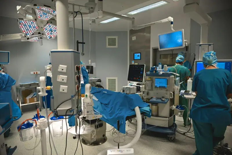 Hospital procedure room with monitors, surgical lights and clinicians in blue scrubs at work