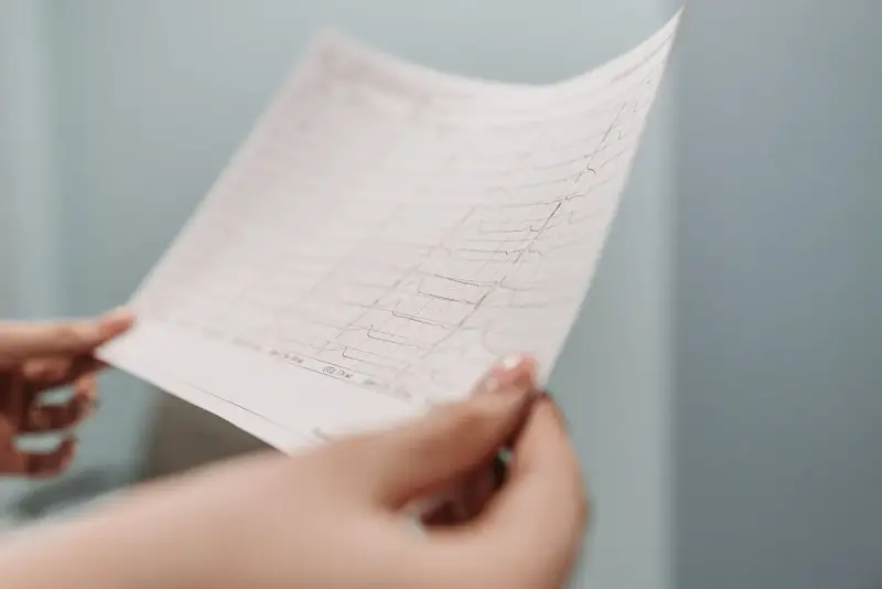 Clinician's hands holding up a printed electrocardiogram tracing for review