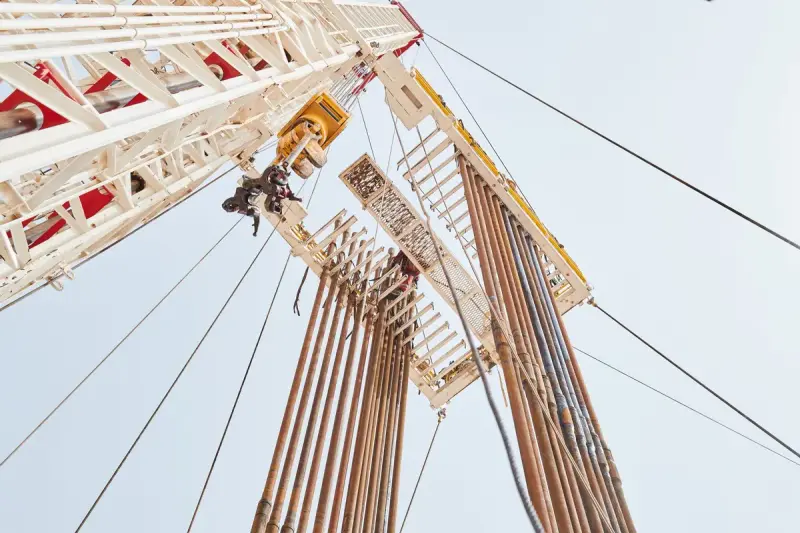 Worker climbing the derrick of a drilling rig seen from below