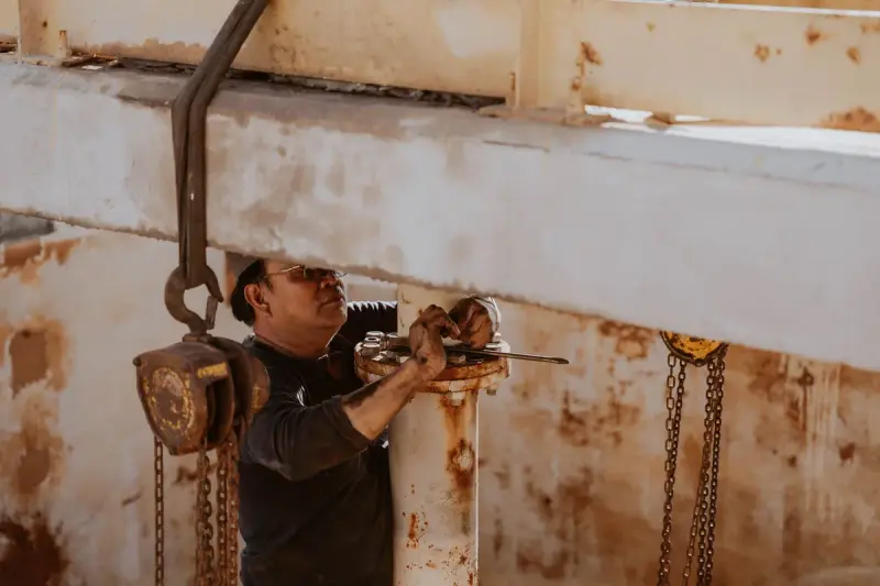 Worker in a hard hat tightening a chain hoist on industrial equipment