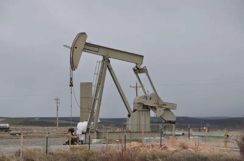 Pumpjack and well-site tanks on flat ground under an overcast sky