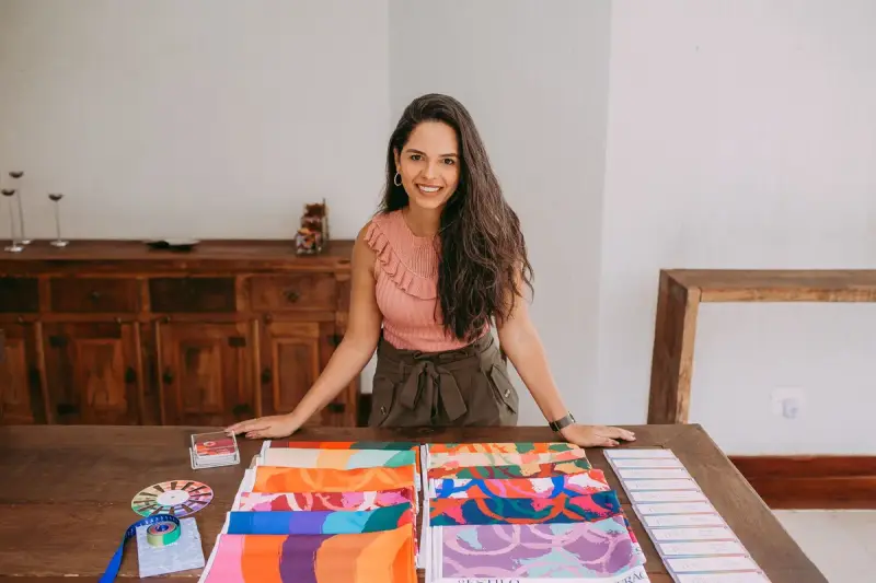 Smiling woman presenting colorful patterned fabric samples spread on a wooden table