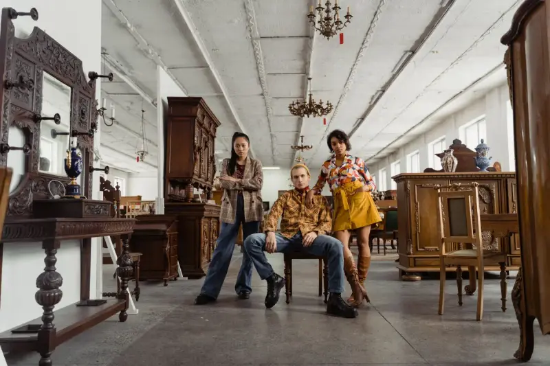 Three people posing among carved wooden cabinets in a large furniture hall