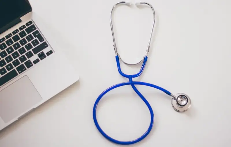 Stethoscope resting beside an open laptop on a white desk