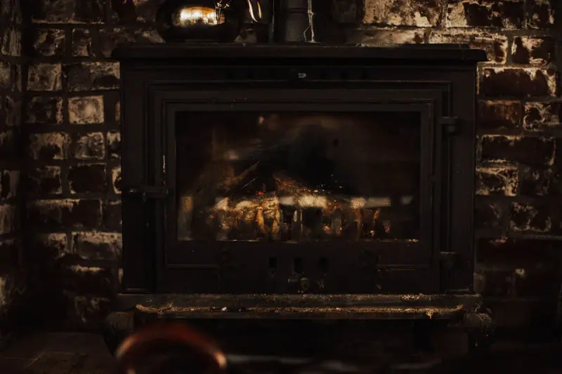 Black cast-iron wood stove with a fire burning against a dark brick wall