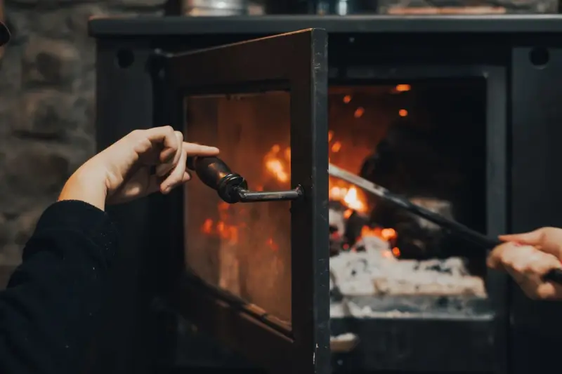 Hand opening the glass door of a burning wood fireplace with a poker