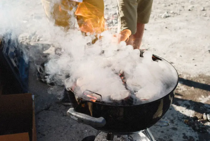 Smoke billowing from a kettle grill as meat cooks outdoors