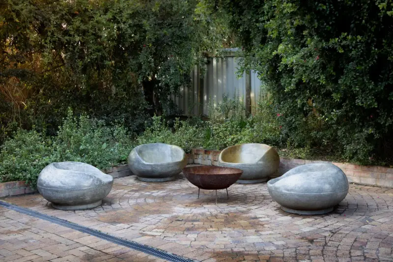 Backyard patio with sculpted stone chairs around a steel fire bowl