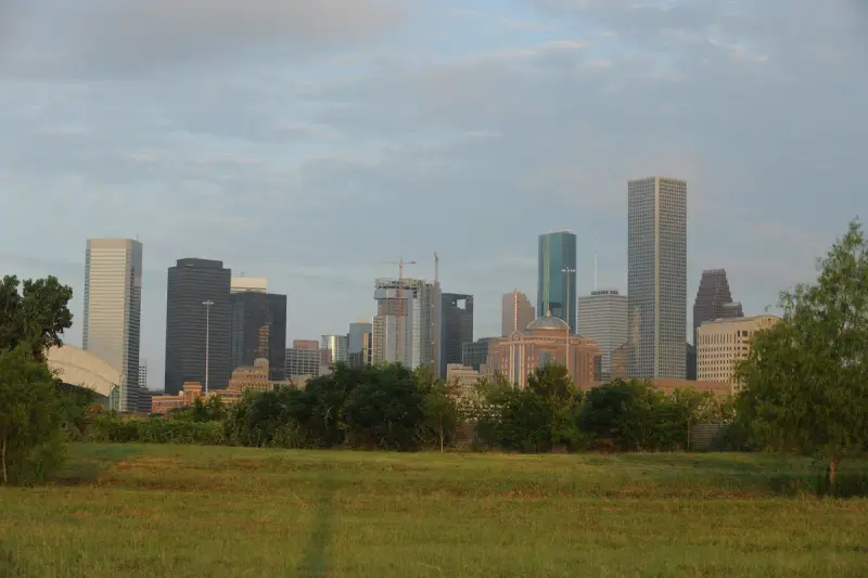 Downtown Houston skyline at sunrise seen across a grassy field near Buffalo Bayou