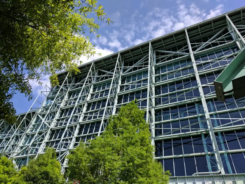 Steel truss and glass curtain wall of the George R. Brown Convention Center in Houston behind green trees