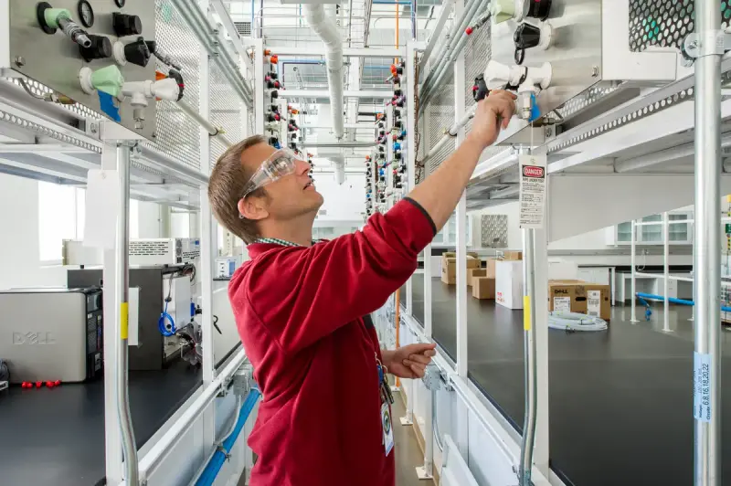 Gas manifold corridor with labeled lines feeding fuel cell test stations in a hydrogen lab
