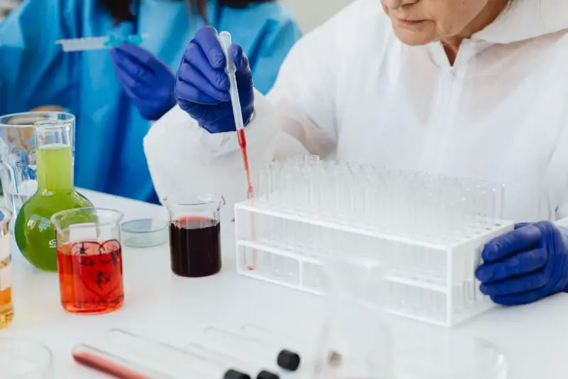 A scientist uses a pipette with test tubes at a laboratory bench.