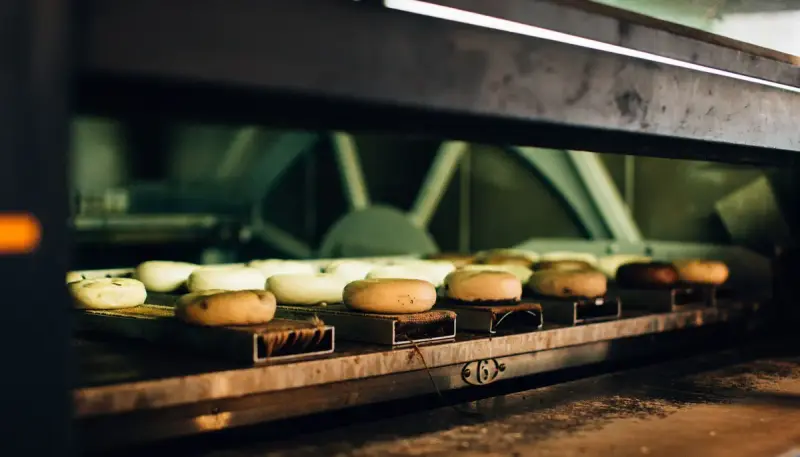 Rows of bagels baking on metal boards inside a commercial bakery oven