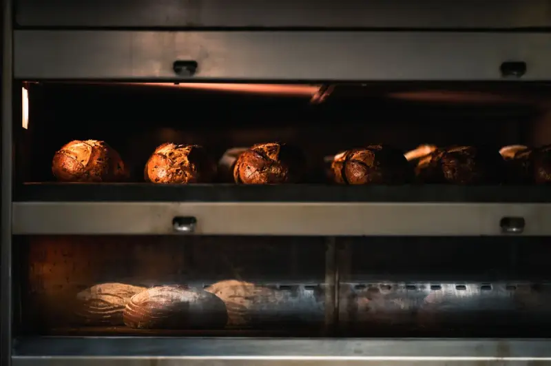 Crusty scored loaves baking on two decks of a stainless steel bakery oven