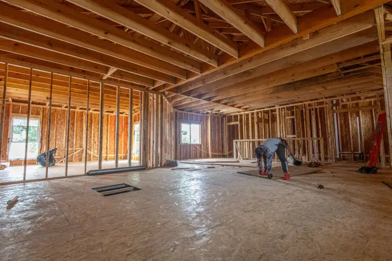 Framed interior of a new Texas home with a worker cutting on the subfloor
