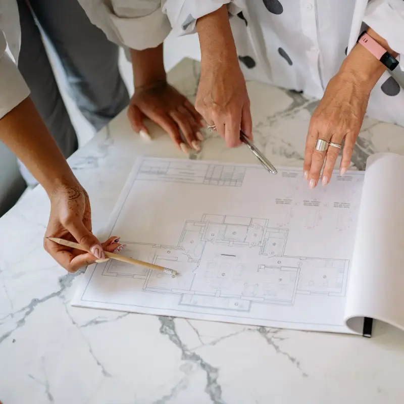 Two women pointing at a house blueprint while planning a build