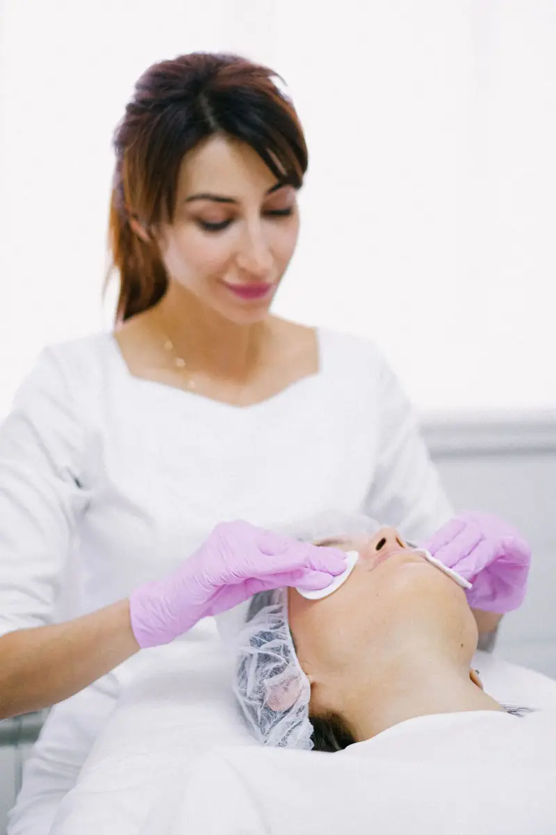 Esthetician in pink gloves cleansing a client's face with cotton pads