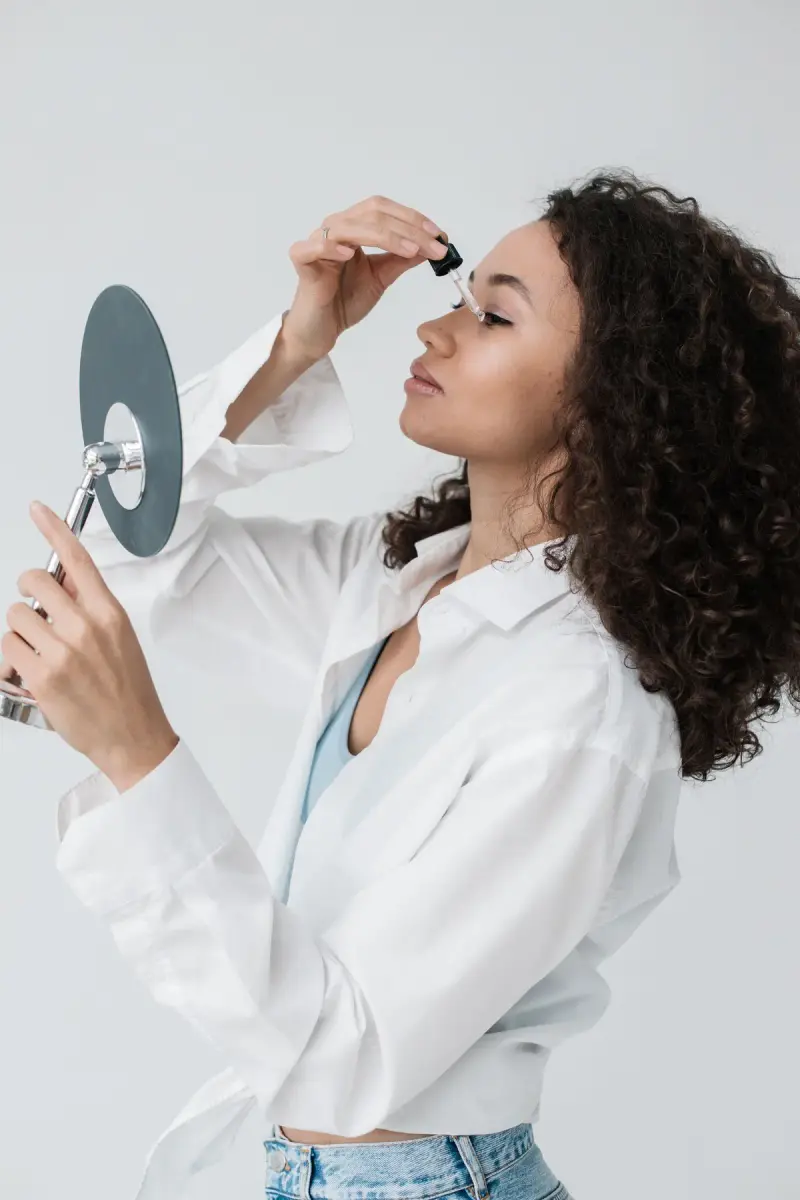 Woman with curly hair applying serum with a dropper at a mirror