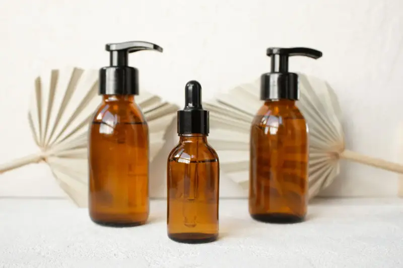 Three amber glass bottles with black pumps and a dropper on a white table