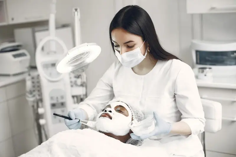 Spa professional applying a facial mask to a client in a modern clinic room