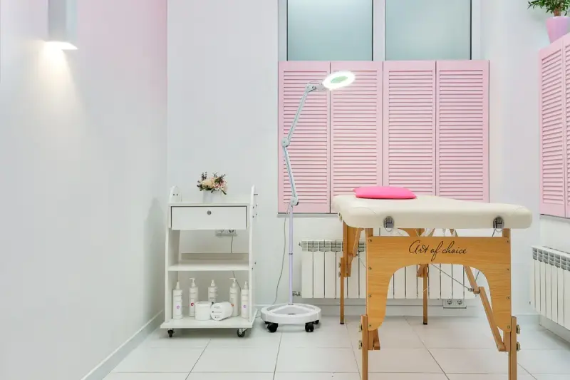 Cosmetology room with a treatment bed under a magnifying lamp and shelves of skincare