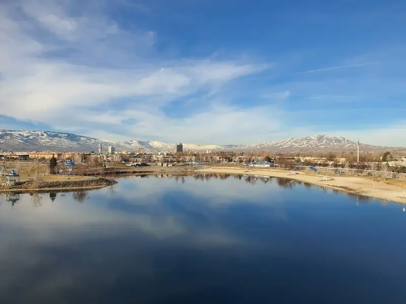 Reno skyline across a still lake with snow-capped Sierra Nevada peaks behind