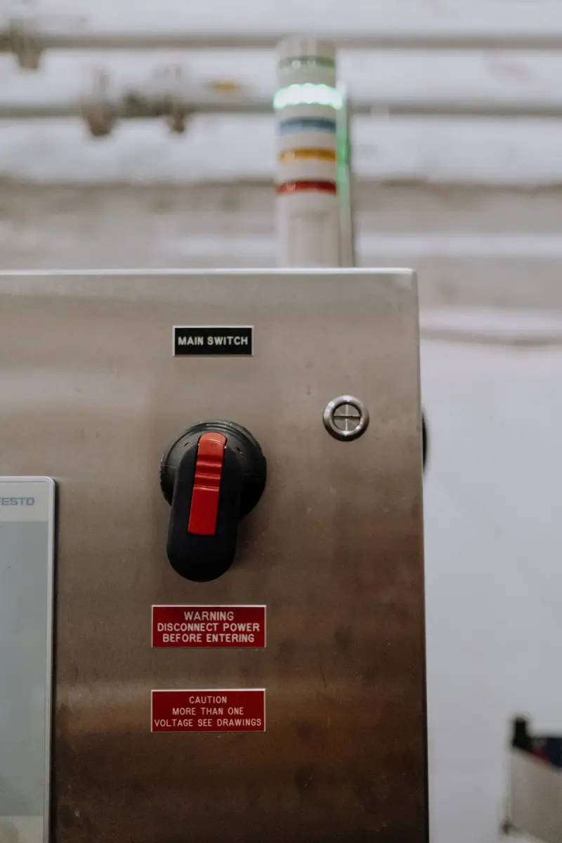 Red main disconnect handle on a stainless control cabinet with safety labels