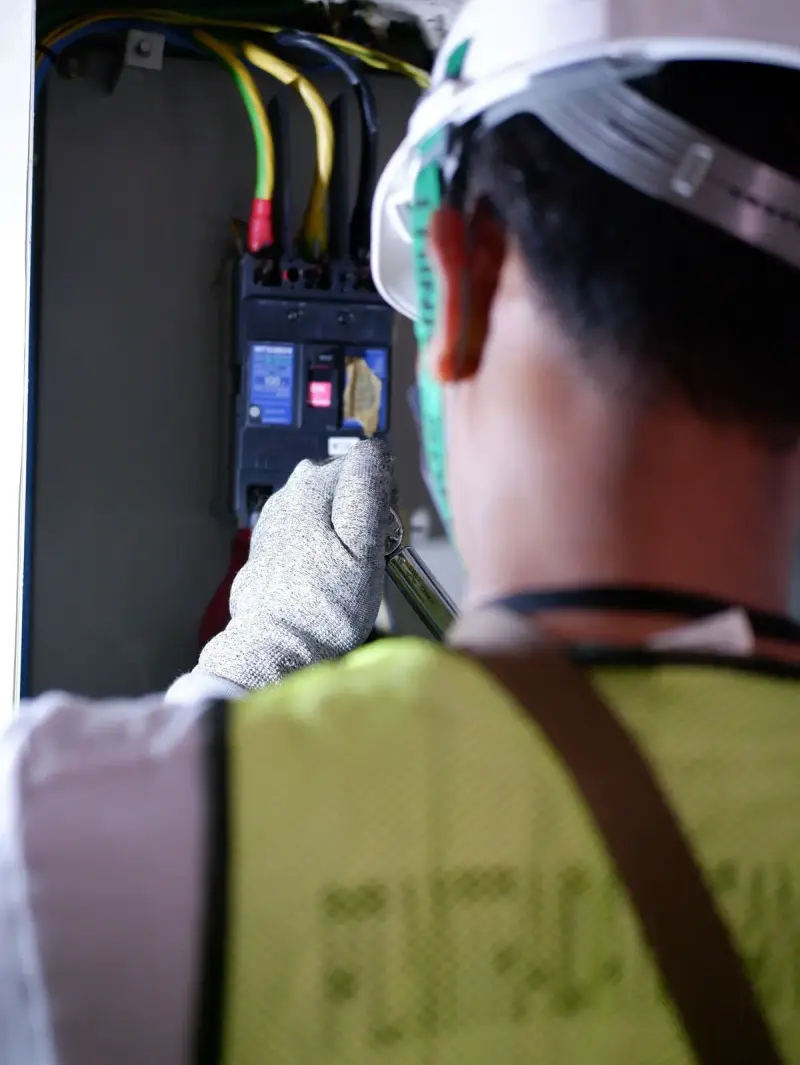 Electrician in a hard hat and gloves operating a circuit breaker in a panel