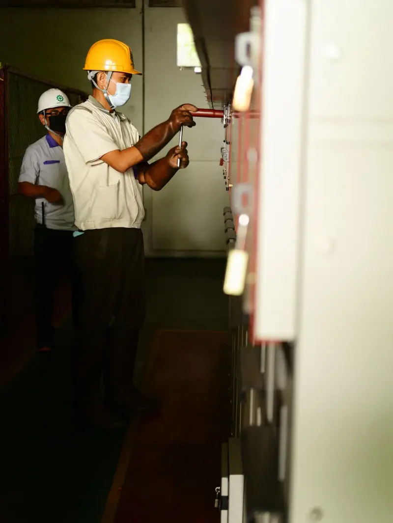 Two electricians in hard hats working along a row of indoor control panels