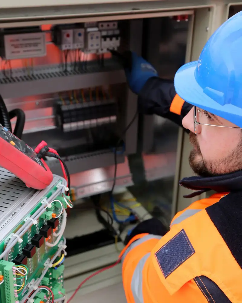 Electrician in hard hat and safety glasses working with test leads in a switchboard