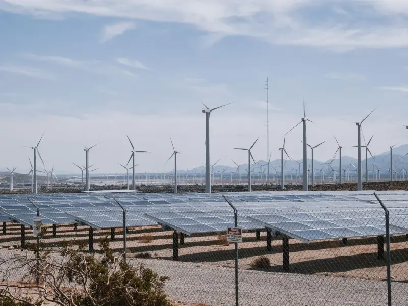Fenced solar field with a line of wind turbines in a desert landscape